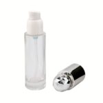 A 1 oz clear glass cylinder treatment bottle featuring a high-precision white pump and a premium transparent diamond-cut overcap. The bottle is shown in a professional studio setting, highlighting the multi-faceted, light-catching properties of the cap.