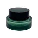 A professional shot of a 1.69 oz (50 ml) low-profile glass jar featuring a thick, heavy base and a sleek black matte lid. The minimalist design highlights the clarity and premium quality of the glass.