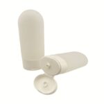 A 100ml matte white oval sunscreen tottle standing upside down on its matching white flip-top dispensing cap.